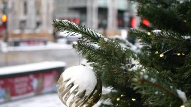 Üzerinde kar olan ladin dalları ve ön planda Noel oyuncakları ve arka planda kış sokağı.