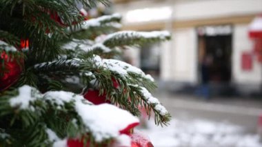 Üzerinde kar olan ladin dalları ve ön planda Noel oyuncakları ve arka planda kış sokağı.