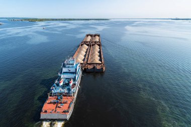 Kum yelkenli büyük bir mavna geniş Volga nehri boyunca sahil boyunca ilerliyor.