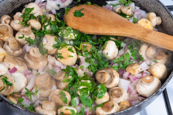 Cooking vegan mushroom fricassee with garlic and onions in a frying pan - garlic mushrooms, French cuisine.