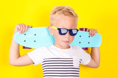 Sevimli güzel sarışın çocuğun kollarına kaykay ile güneş gözlüğü takıyor Sarı zemin üzerine parlak portpait