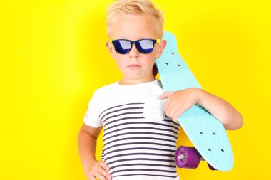 Sevimli güzel sarışın çocuğun kollarına kaykay ile güneş gözlüğü takıyor Sarı zemin üzerine parlak portpait