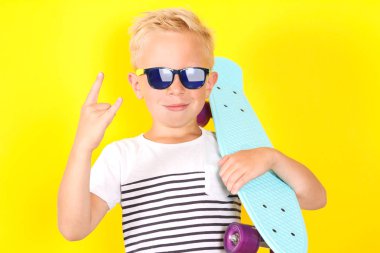 Sevimli güzel sarışın çocuğun kollarına kaykay ile güneş gözlüğü takıyor Sarı zemin üzerine parlak portpait