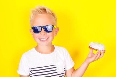 Hoş serin sarışın çocuk güneş gözlüğü ve enjoing çörek sarı arka plan üzerinde parlak portpait