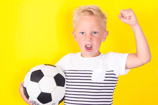 サッカー ゲームをロック黄色の背景の上にボールを持つかわいい金髪の少年の肖像画 — ストック写真
