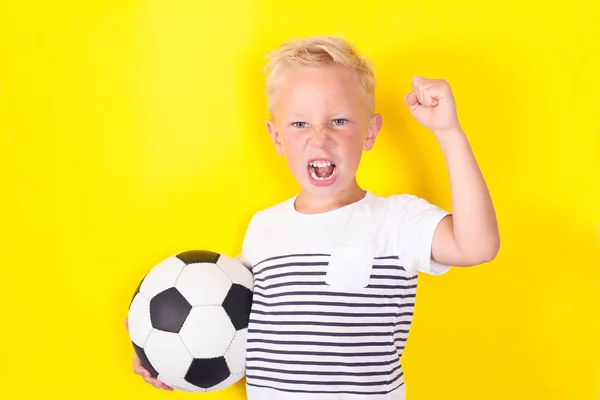 サッカー ゲームをロック黄色の背景の上にボールを持つかわいい金髪の少年の肖像画 — ストック写真