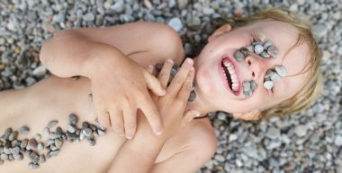 Güneşli kumsalda mutlu çocuklar eğleniyor, sıcak çakıl taşına uzanıp güneşleniyor, denizde yüzdükten sonra ısınıyorlar. Aktif çocuk yaşam tarzı, çocuklarla tropik aile tatil beldesinde yaz tatili..