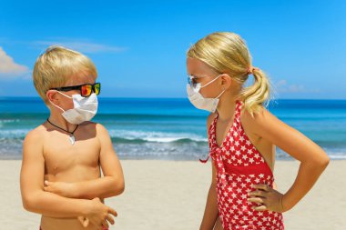 Deniz sahilinde güneş gözlüğü takan, koruyucu maskeli iki komik çocuk. Yaz turları, Coronavirus COVID-19 dünya salgını nedeniyle gemi seyahatleri iptal. Aile tatili için güvenli seyahat yerleri