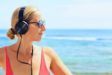 Kulaklıklı, güneş gözlüklü, müzik dinleyen ve rahatlatan genç bir kız. Tropik deniz sahillerinde takılan bir kadın. Seyahat aile hayatı, yaz tatillerinde eğlence aktiviteleri..