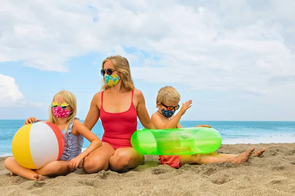 Funny children in sunglasses, inflatable toys on tropical sea beach. New rules to wear cloth face covering mask at public places due coronavirus COVID 19. Family holidays with children, summer travel