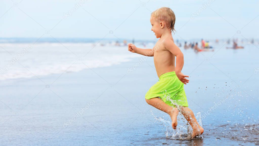 Happy family have fun on tropical sea beach resort. Funny baby boy run with splashes by water pool along surf edge. Active kids lifestyle, people swimming activity on summer holiday with children.