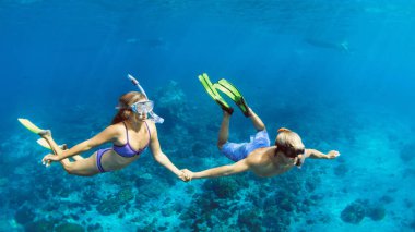 Mutlu aile tatilleri. Şnorkelli genç çift el ele tutuşuyor, mercan resiflerindeki deniz havuzunda balıklarla serbest dalış yapıyorlar. Seyahat yaşam tarzı, su sporları macerası, yaz tatilinde yüzme etkinliği.