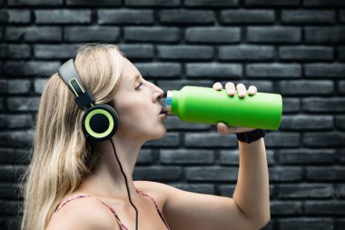 Siyah arka plandaki genç sarışın kadın yeşil kullanılabilir şişeden taze kaynak suyu içiyor. Yaz şehrinde sağlıklı bir yaşam tarzı.