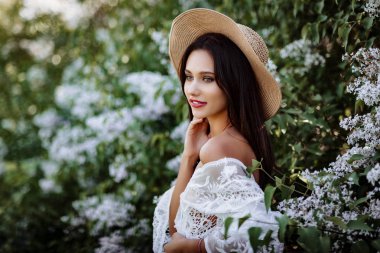 Leylak rengi şapkalı genç bir kadın. Çiçekler arasında beyaz pennuar modeli