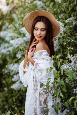 Leylak rengi şapkalı genç bir kadın. Çiçekler arasında beyaz pennuar modeli