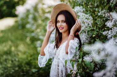 Leylak rengi şapkalı genç bir kadın. Çiçekler arasında beyaz pennuar modeli