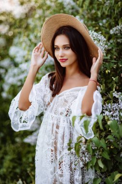 Leylak rengi şapkalı genç bir kadın. Çiçekler arasında beyaz pennuar modeli