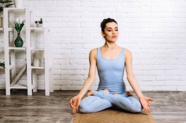 Yoga yapan genç bir Yogi kadını. Mavi spor kıyafetli kız paspasın üzerinde pilates yapıyor.