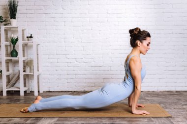 Yoga yapan genç bir Yogi kadını. Mavi spor kıyafetli kız paspasın üzerinde pilates yapıyor.