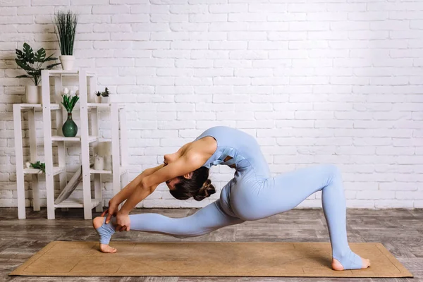 Yoga yapan genç bir Yogi kadını. Mavi spor kıyafetli kız paspasın üzerinde pilates yapıyor.