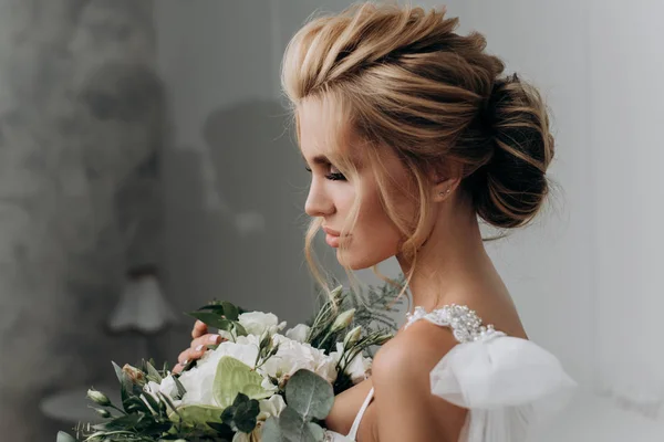 Наречена з красивою зачіскою. Модель блондинки в весільній сукні в білому інтер'єрі — стокове фото