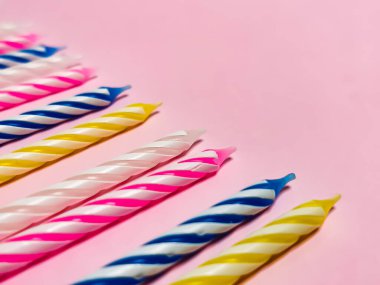 Pembe arka planda çok renkli doğum günü mumlarının yakın çekimi. Tebrik kartı için boşluk, doğum günü davetiyesi için geçmiş bayram ve partinin sembolü. Seçici odak.