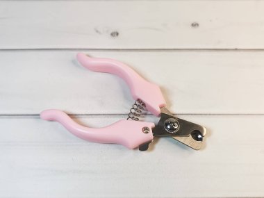 Hafif ahşap arka planda pembe saplı evcil hayvan tırnak makası. Kedi ve köpeklerin hijyenik bakımı için tımar aletleri..