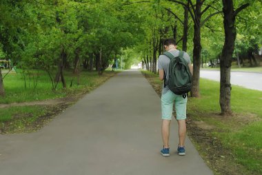 Kısa şortlu genç bir adam telefonda mesajları kontrol etmek ya da bir harita görmek için durdu. Fotoğraf, bir yaz günü arkadan çekildi. Şehirde tek başına dolaşmak..