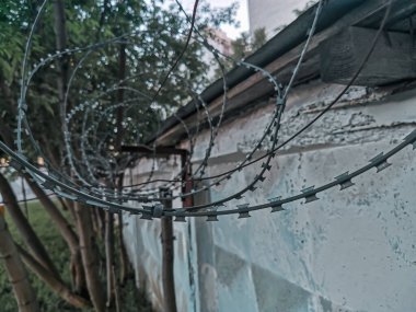 Dikenli telli beton çit. Dikenli tellere yakın çekim. Şehir içindeki özel koruma alanları: askeri üs, hapishane. Özgürlük kavramı. Kablonun ön planına seçici odaklanma, tonlama.