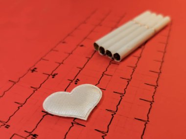 Sigara arkaplanındaki beyaz bir kalp kardiyogramın kırmızı çıktısında yatıyor. Kalbe tütün içmenin zararının sembolü. Tütün günü yok. Beyaz bir kalbe odaklan