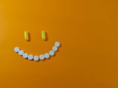 Turuncu arka plandaki haplardan yapılmış neşeli bir gülümseme. İyileşme konsepti, depresyonun üstesinden gelme, sağlık. Metin veya logo için boşluk