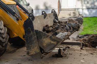 Toprak ve asfalt parçalarıyla dolu büyük bir buldozer kovası. Şehir kanalizasyon ve yeraltı iletişimi için inşaat makineleri ve ekipmanlar.