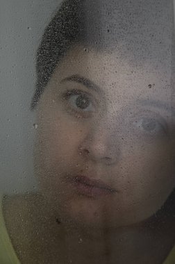 Camların arkasında yağmur damlalarıyla genç esmer kadının dikey portresi. Depresyon konsepti, gelecek hakkında bulanıklık, kararlılık. Cama damlalara odaklan..
