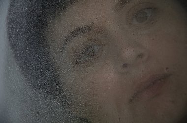 Bardağın arkasında yağmur damlaları olan esmer bir kadının portresi. Depresyon konsepti, gelecek hakkında bulanıklık, kararlılık. Cama damlalara odaklan..