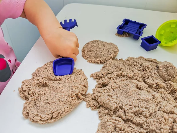 Child plays with kinetic sand: closeup of a child\'s hand and sand. Educational games with children for fine motor skills. Kinetic sand is a natural color. Selective focus on child\'s hand with scapula