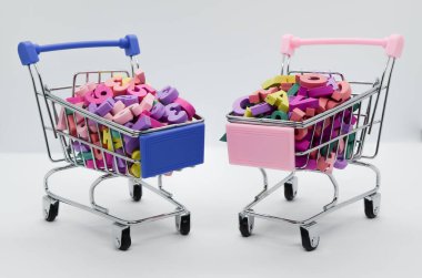 Beyaz arka planda iki süpermarket vagonunda çok renkli tahta harfler ve numaralar var. Mesaj için yer var. Matematiksel ve insani zihniyetlerin karşılaştırılması. Konsept: okula dönüş.