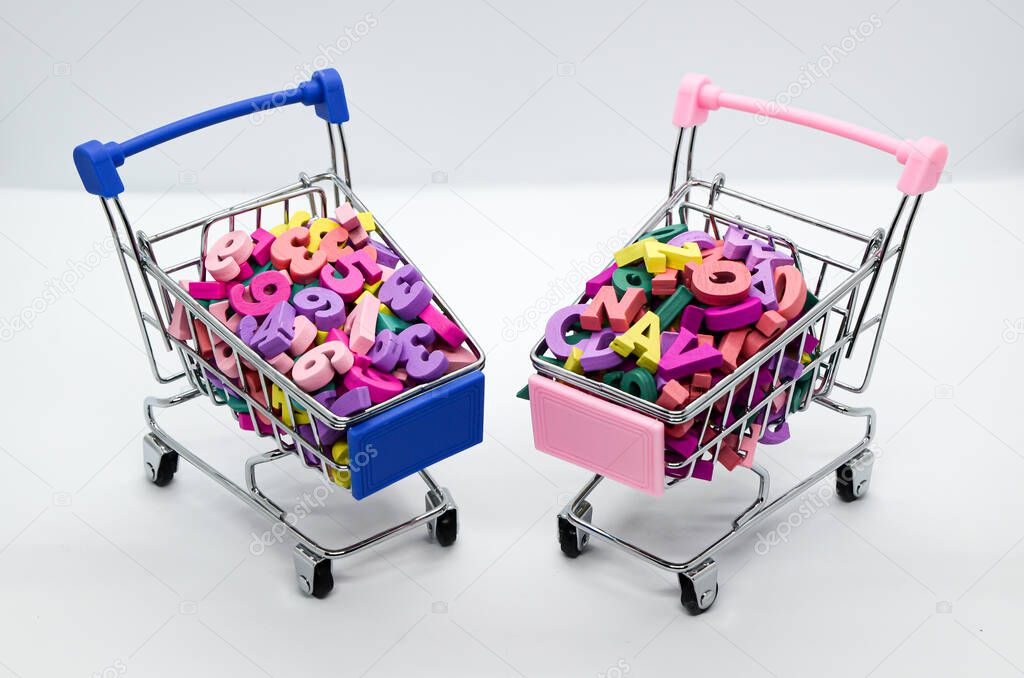 Multicolored wooden letters and numbers in two supermarket trolleys on white background. Space for text. Comparison of mathematical and humanitarian mindset. Concept: back to school.