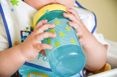 Bir yaşındaki bir çocuk iki eliyle su geçirmez bir kase tutuyor. Bebek elleri yakın plan. Bebek beslenmesi..