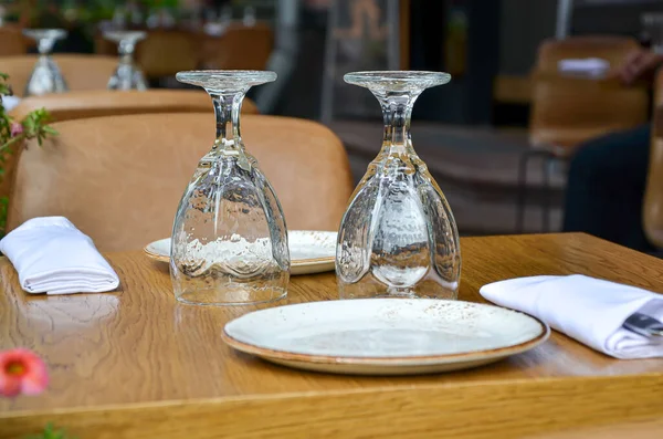 Table on the veranda of the restaurant, served for two: two inverted glasses, napkins and cutlery on a wooden table. Restaurant business, table setting and cafe design.