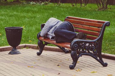 Sıcak kıyafetler giymiş evsiz bir adam metropolün parkında açık hava bankında uyuyor. Sosyal sorunlar, kriz ve terk etme, yoksulluk