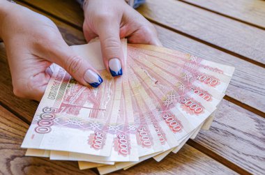 Manikürlü bir kadın eli, ahşap bir masanın arka planında beş bininci Rus rublesi fanı tutuyor. Nakit ödemeler, büyük faturalar..