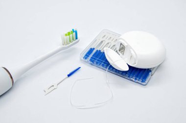 Ağız bakımı: elektrikli diş fırçası, diş ipi ve beyaz arka plandaki interdental alanlar için fırçalar. Diş bakımı, ağız hijyeni. Konsept: Diş hizmetleri, ağız sağlığı, diş bakımı.