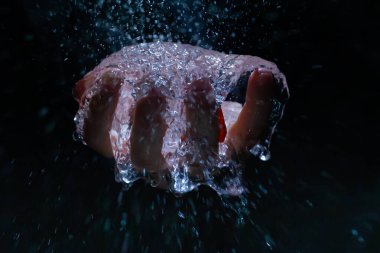 Bir elinde su dolu plastik bir balonun patlaması ve siyah bir arka plan.