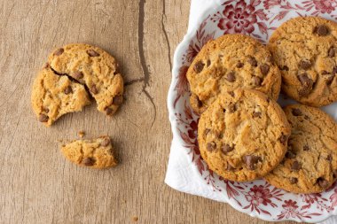 Çikolata parçacıklı ve vanilyalı kurabiyeler, ahşap bir masanın üzerinde kırık kurabiyeyle süslenmiş bir tabakta..