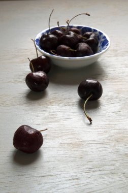 Siyah kirazlar beyaz ve mavi bir kasede, ahşap masanın üzerinde..