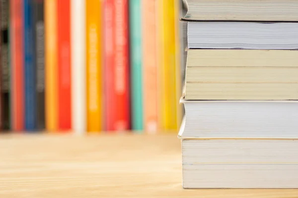 Pile of books in front of unfocused books over a wooden table.