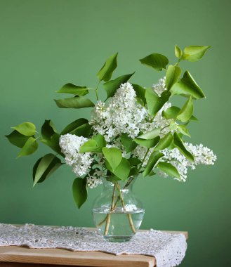 Beyaz Lila. Çiçekli dallar yeşil bir arka plan üzerinde bir masada bir cam vazoda buket.
