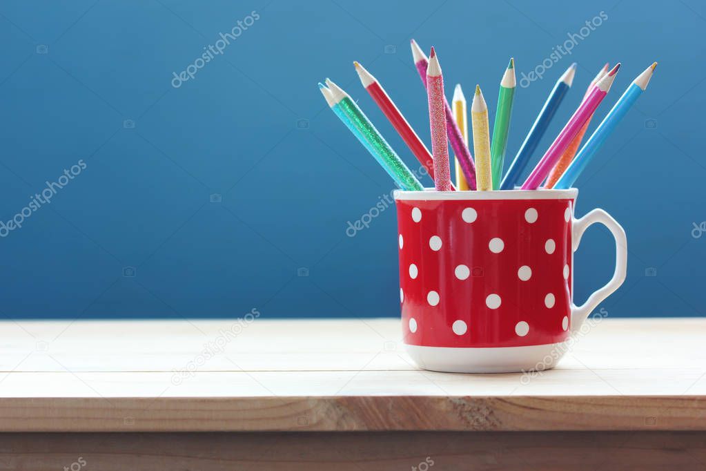 Mug with colored pencils on a wooden table on a blue background. Creativity, education, drawing, space for text.