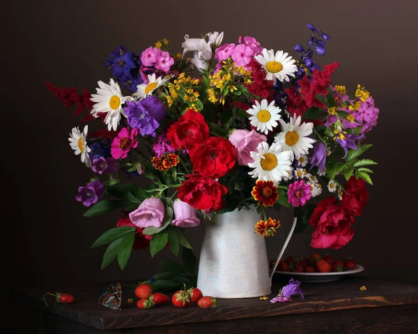 Bir sürahi ve karanlık bir arka plan üzerinde çilek Bahçe çiçek bir buket ile natürmort.