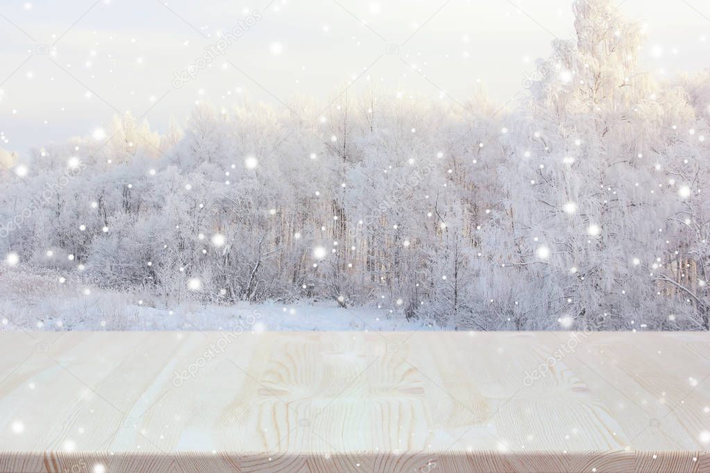Empty wooden table on blurred winter backdrop. Empty space for Your object. Light background, table layout with winter trees and snowflakes.